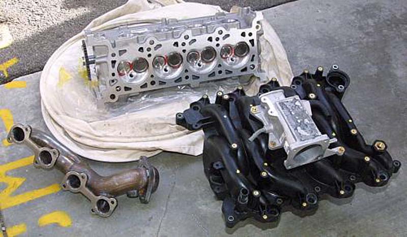 Aluminum SOHC cylinder head, cast-iron exhaust manifold and black intake manifold on concrete