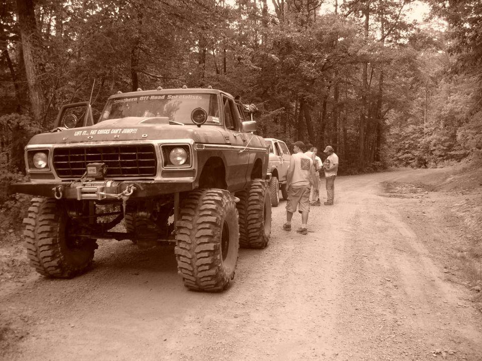 Modified Ford F-Series truck with large tires and winch, parked on a dirt road