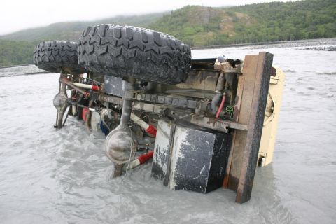 2003 Jeep TJ - An overturned vehicle lies submerged in a river, its tires and undercarriage exposed to the elements.