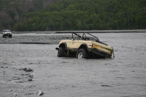 2003 Jeep TJ - A tan SUV is partially submerged and stuck in a river, with a white SUV visible in the distance.