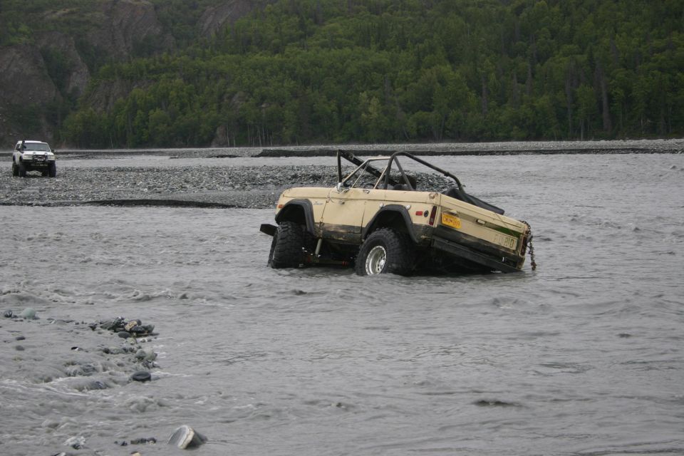 Tan SUV stuck in a river with another white SUV in the background