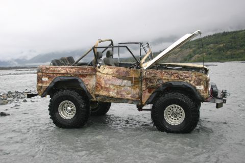 2003 Jeep TJ - This heavily rusted Ford Bronco is parked in shallow water with its hood up.