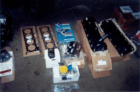 1992 Ford Crown Victoria - New engine parts laid out on a concrete garage floor: a pair of multi-layer head gaskets, a black valve cover and oil pan still in their op…