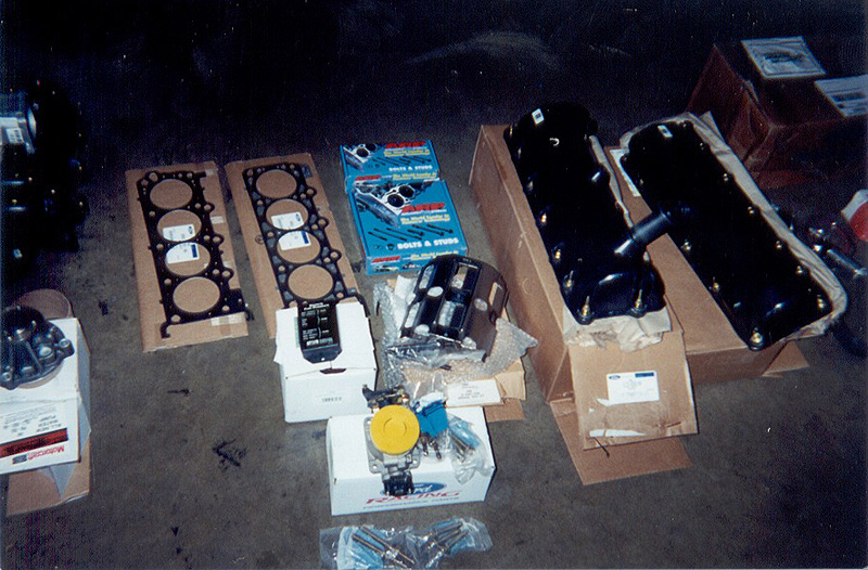 Ford engine rebuild parts on garage floor: head gaskets, valve cover, oil pan, ARP bolts