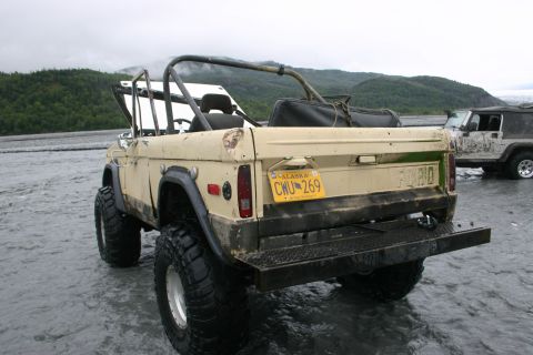 2003 Jeep TJ - A tan Ford Bronco with a roll cage and large tires is parked in shallow water, with another Jeep visible in the background.