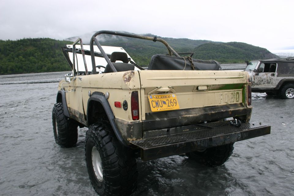 Tan Ford Bronco with roll cage and large tires parked in shallow water