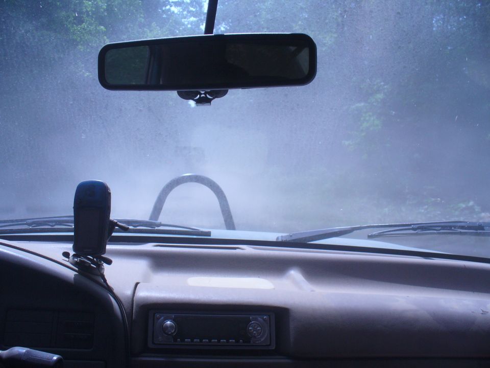 Interior view from driver's seat looking through windshield at a roll bar and dusty conditions