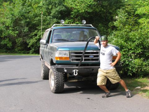 1995 Ford C-350 (Centurion Conversions) - A man poses next to a lifted green SUV on a paved road with trees behind.
