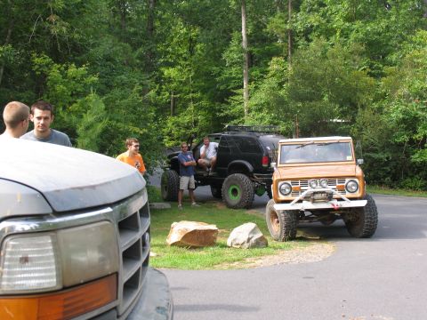 1995 Ford C-350 (Centurion Conversions) - A tan Ford Bronco is parked on a paved area with a wooded background, showing off its off-road modifications.