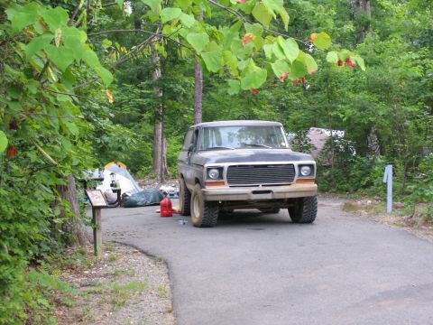1995 Ford C-350 (Centurion Conversions) - A Ford Bronco sits parked at a campsite with tents and camping gear nearby.