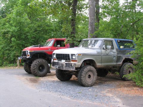 1995 Ford C-350 (Centurion Conversions) - Two heavily modified Ford trucks, a Bronco and a pickup, are parked off-road in a wooded area.