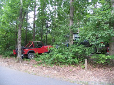 1995 Ford C-350 (Centurion Conversions) - A red Jeep Wrangler and a dark SUV are parked in a wooded area.