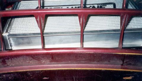 1992 Ford Crown Victoria - Close-up looking down through the dark red grille and header panel of a car at a bare aluminum heat exchanger core stacked in front of the…