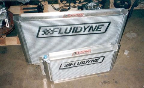 1992 Ford Crown Victoria - Two aluminum Fluidyne radiators standing side by side on a garage floor, a tall one behind and a shorter, wider one in front with a blue-an…