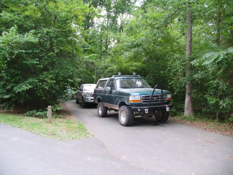 1995 Ford C-350 (Centurion Conversions) - A modified 1995 Ford Bronco is parked on a paved road, with another vehicle behind it, surrounded by trees.