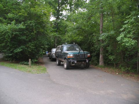 1995 Ford C-350 (Centurion Conversions) - A modified 1995 Ford Bronco is parked on a paved road surrounded by trees, with another vehicle behind it.