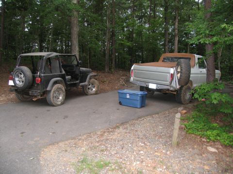 1995 Ford C-350 (Centurion Conversions) - Two vehicles, a Jeep and a Ford pickup, are parked on a road in a wooded area with a blue storage bin nearby.