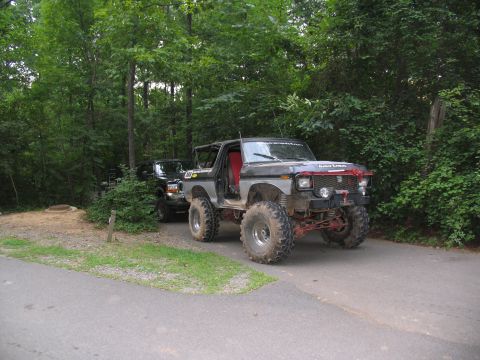 1995 Ford C-350 (Centurion Conversions) - Modified 1978 Ford Bronco with off-road modifications, parked beside a black SUV in a wooded area.