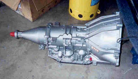 1992 Ford Crown Victoria - A freshly rebuilt aluminum automatic transmission lying on a concrete garage floor, bellhousing at right and tailshaft with a red shipping…
