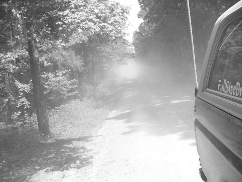 1996 Ford Bronco - Driving down a dusty road through trees, with part of a vehicle visible on the right.