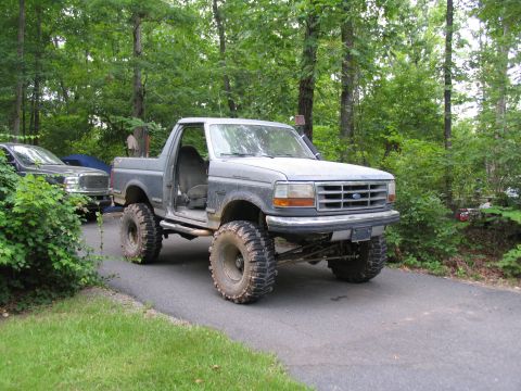 1995 Ford C-350 (Centurion Conversions) - Modified gray Ford Bronco with off-road tires sits parked on a driveway next to another vehicle.
