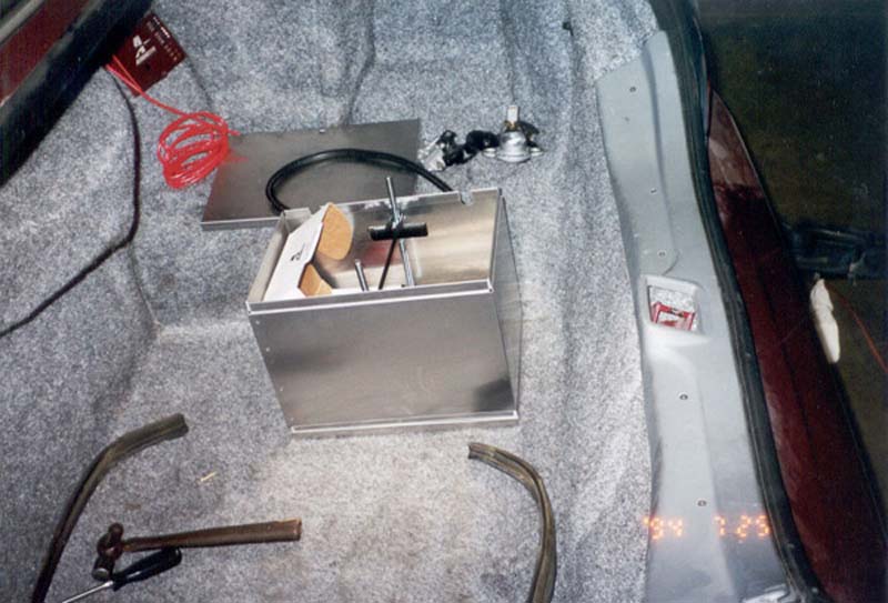 Aluminum trunk battery box with hold-down and red cable in a carpeted car trunk