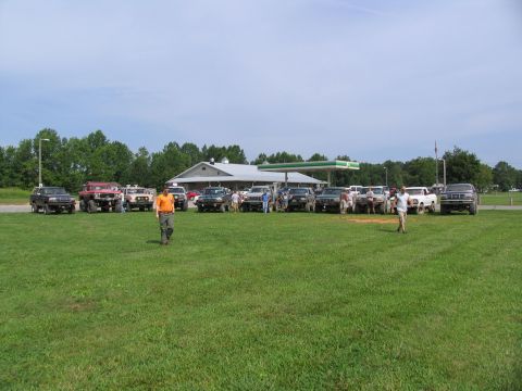 1995 Ford C-350 (Centurion Conversions) - A group of off-road vehicles are gathered at a gas station on a sunny day.