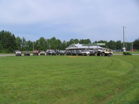 1995 Ford C-350 (Centurion Conversions) - A group of off-road vehicles are parked in a field by a gas station.