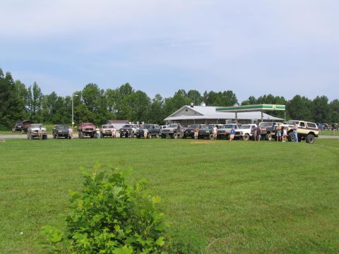 1995 Ford C-350 (Centurion Conversions) - A group of off-road vehicles are gathered in a field near a gas station.