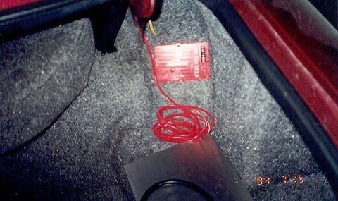 1992 Ford Crown Victoria - A red anodized electronic control module mounted to the gray carpeted floor of a car trunk, with a yellow trigger wire at top and a coil of…