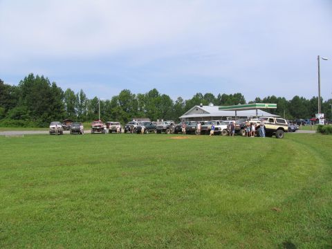 1995 Ford C-350 (Centurion Conversions) - A group of off-road vehicles are gathered in a field next to a gas station.