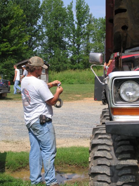 1995 Ford C-350 (Centurion Conversions) - Man works on a large truck with oversized tires in an outdoor setting.