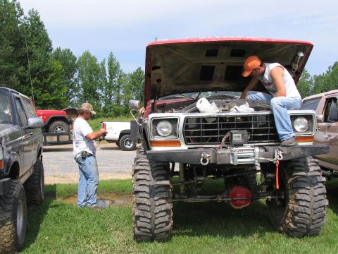 1995 Ford C-350 (Centurion Conversions) - Two men attend to a heavily modified pickup truck with its hood open, parked outdoors on a sunny day.