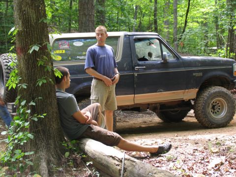 1995 Ford C-350 (Centurion Conversions) - Two men converse near a lifted Ford Bronco during an outdoor excursion in a forest.