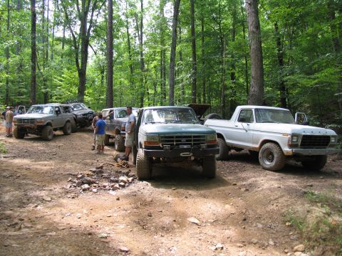 1995 Ford C-350 (Centurion Conversions) - A group of off-road vehicles are parked on a dirt trail surrounded by trees.
