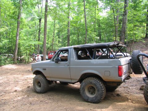 1995 Ford C-350 (Centurion Conversions) - Modified SUV with large tires parked on a dirt trail surrounded by trees.