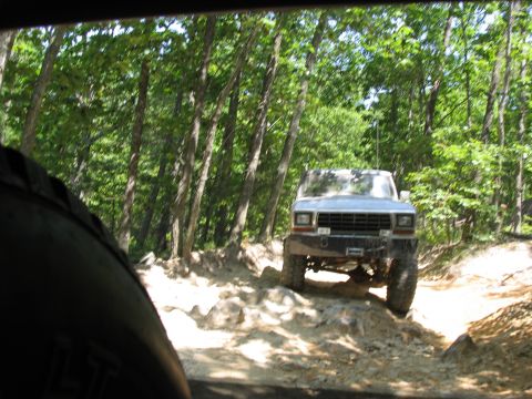 1995 Ford C-350 (Centurion Conversions) - Silver Ford F-Series truck navigates a challenging, rocky off-road trail through a dense forest.