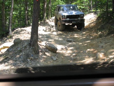 1995 Ford C-350 (Centurion Conversions) - A silver SUV navigates a rocky, wooded trail during an off-road excursion.