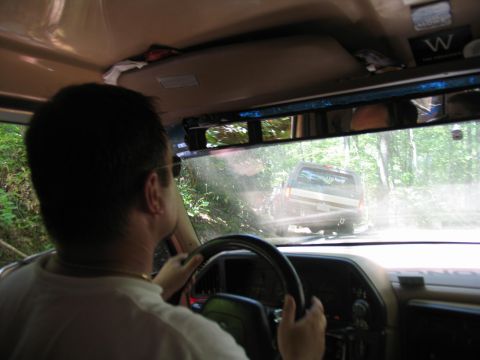 1995 Ford C-350 (Centurion Conversions) - Driving on a dirt road behind another vehicle, surrounded by trees.