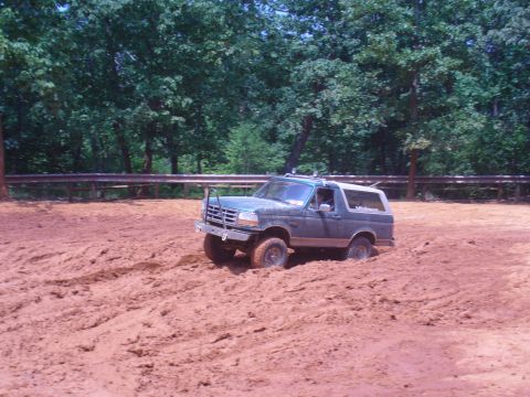1996 Ford Bronco - A Ford Bronco navigates a muddy terrain with trees in the background.