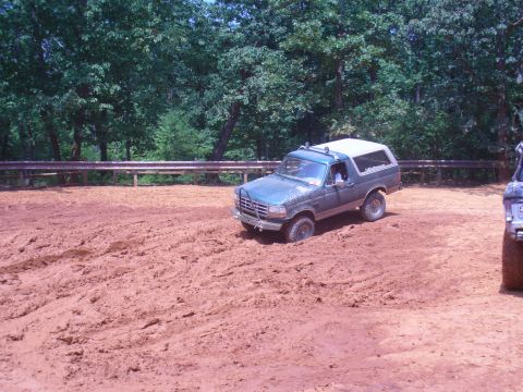 1996 Ford Bronco - A 1996 Ford Bronco is stuck in thick mud, with trees and a guardrail in the background.