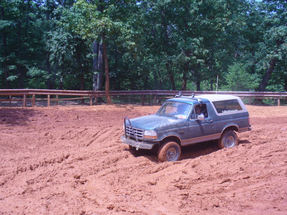 Green 1996 Ford Bronco driving through a muddy area with trees in the background
