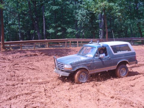 1996 Ford Bronco - A Ford Bronco navigates a muddy off-road course with trees in the background.
