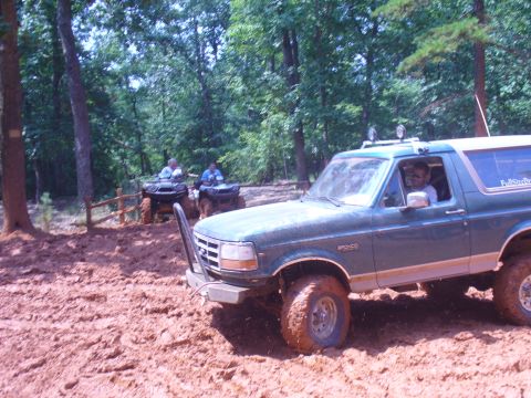 1996 Ford Bronco - A green 1996 Ford Bronco navigates a muddy trail, with ATVs visible in the background.