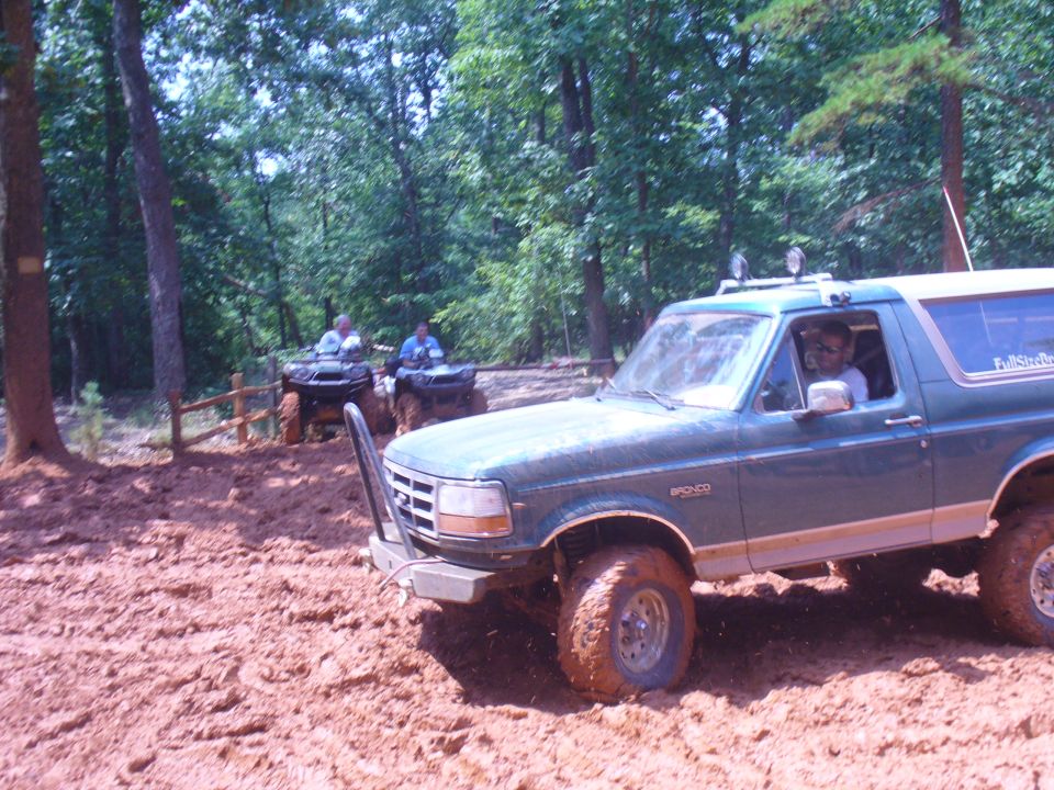 1996 Ford Bronco driving through mud with ATVs