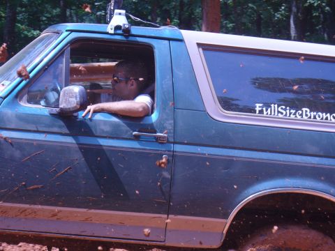 1996 Ford Bronco - A man drives a green Ford Bronco through a muddy, wooded area, with dirt and leaves flying.