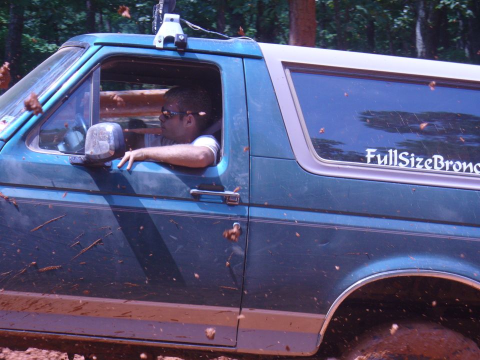 Man driving a green Ford Bronco off-road, mud flying