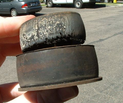 1992 Ford Crown Victoria - A hand holds two rubber suspension bushings for comparison: a worn, cracked and collapsed one on top and a newer, intact replacement below.…