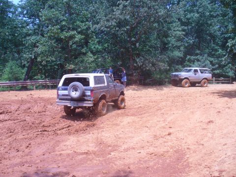 1996 Ford Bronco - Two Ford Broncos navigate a muddy off-road course on a summer day.