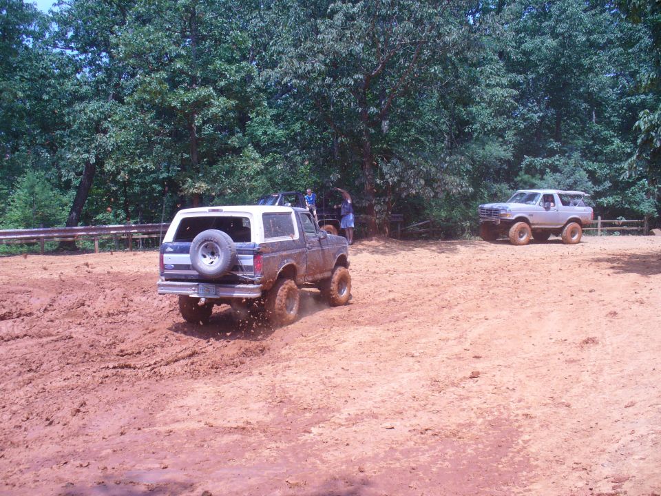 Rear view of a brown 1987 Ford Bronco driving on a muddy track with another Bronco in the background